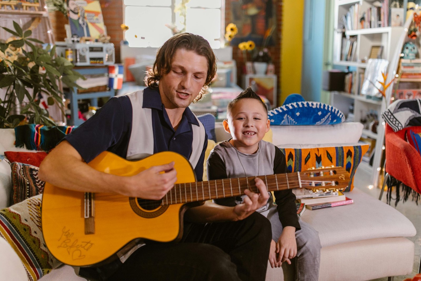 Father and son sharing a musical moment with an acoustic guitar in a cozy living room.